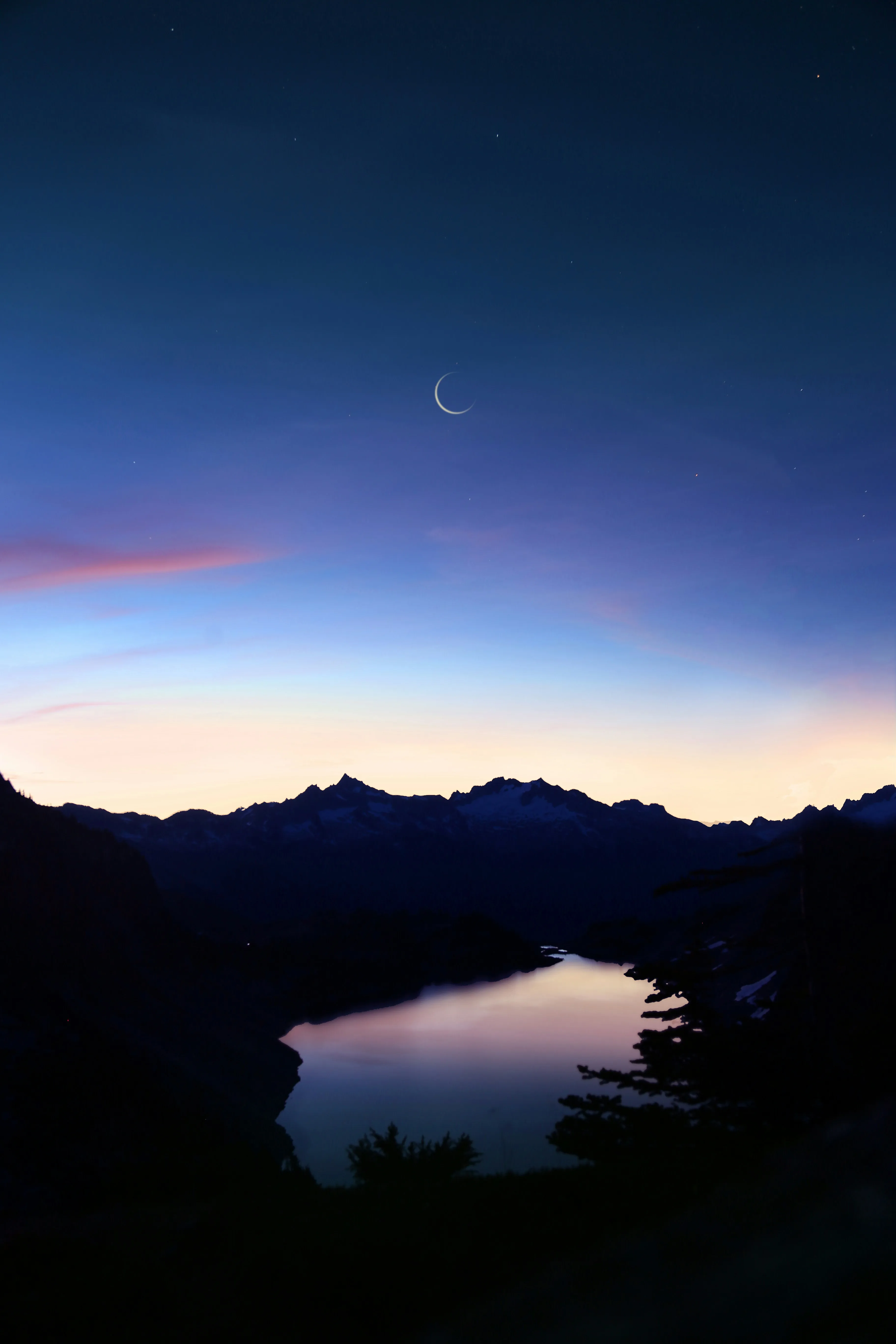 Crescent moon over a mountain lake at twilight